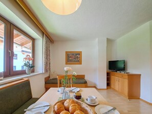 Un coin repas avec une table dressée pour deux personnes, un téléviseur et une fenêtre donnant sur des immeubles.