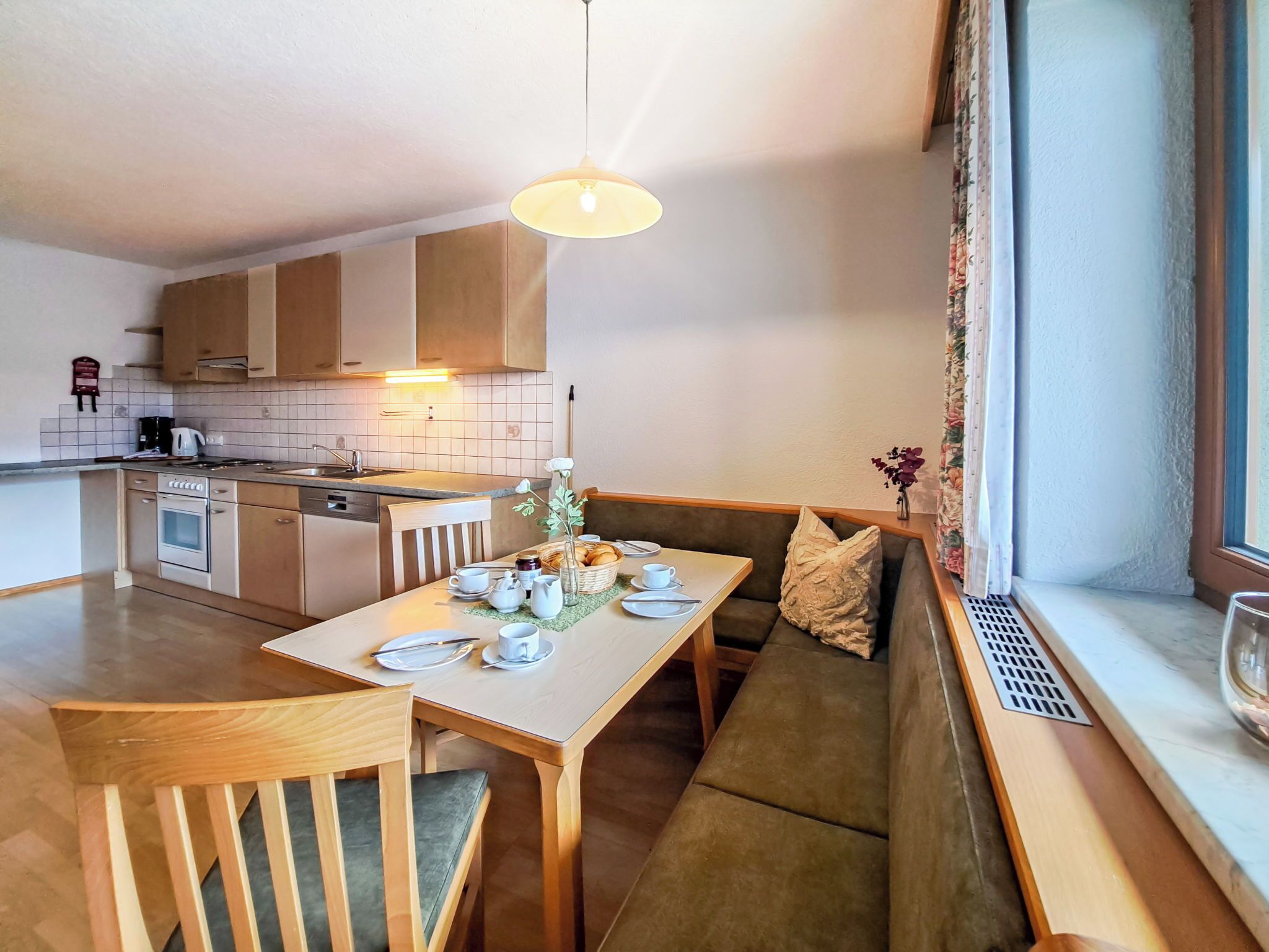 A modern kitchen with a dining area, wooden furniture, and a window with curtains.