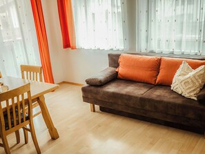 En stue med en brun sofa, orange puder, et træspisebord og en stol.