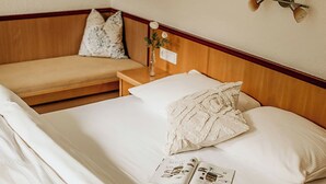 Een net opgemaakt bed met witte lakens, een nachtkastje met een lamp en een wandlamp.