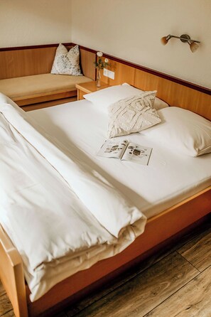 Un lit bien fait, avec du linge de lit blanc, une table de chevet avec une lampe et un luminaire fixé au mur.