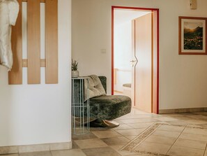 A hallway with a wooden panel wall, a grey sofa, a small table with a plant, and a door leading to another room.
