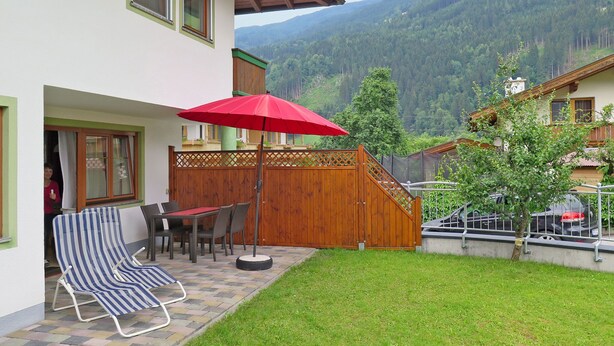 A patio with a table, chairs, and a red umbrella.