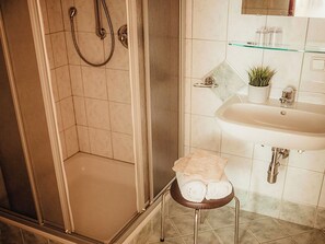 Ein Badezimmer mit Dusche, Waschbecken und einem kleinen Hocker mit Handtüchern.