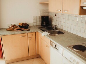 Una cocina con mostrador, pileta, cafetera y muebles bajos de madera.