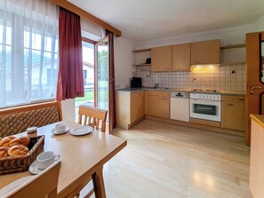 A compact kitchen with wooden cabinets, a built-in oven, and a dining area with a table set for two. - Kraftreich Apartments by Interhome (Zell am Ziller)