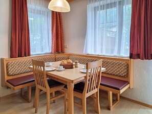 A dining area with a wooden table, four chairs, a bench, and a window with curtains.
