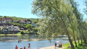 A riverside setting with canoes, people engaging in water activities, and a backdrop of houses and greenery.
