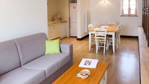 A modern apartment with a grey sofa, wooden dining table, and a kitchen area.
