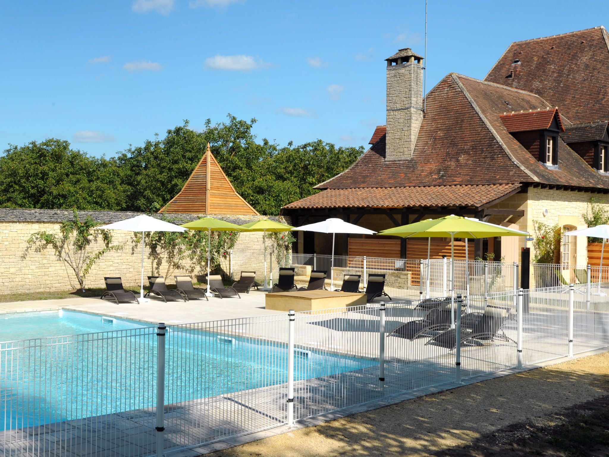 A swimming pool with lounge chairs and umbrellas, surrounded by a fence.
