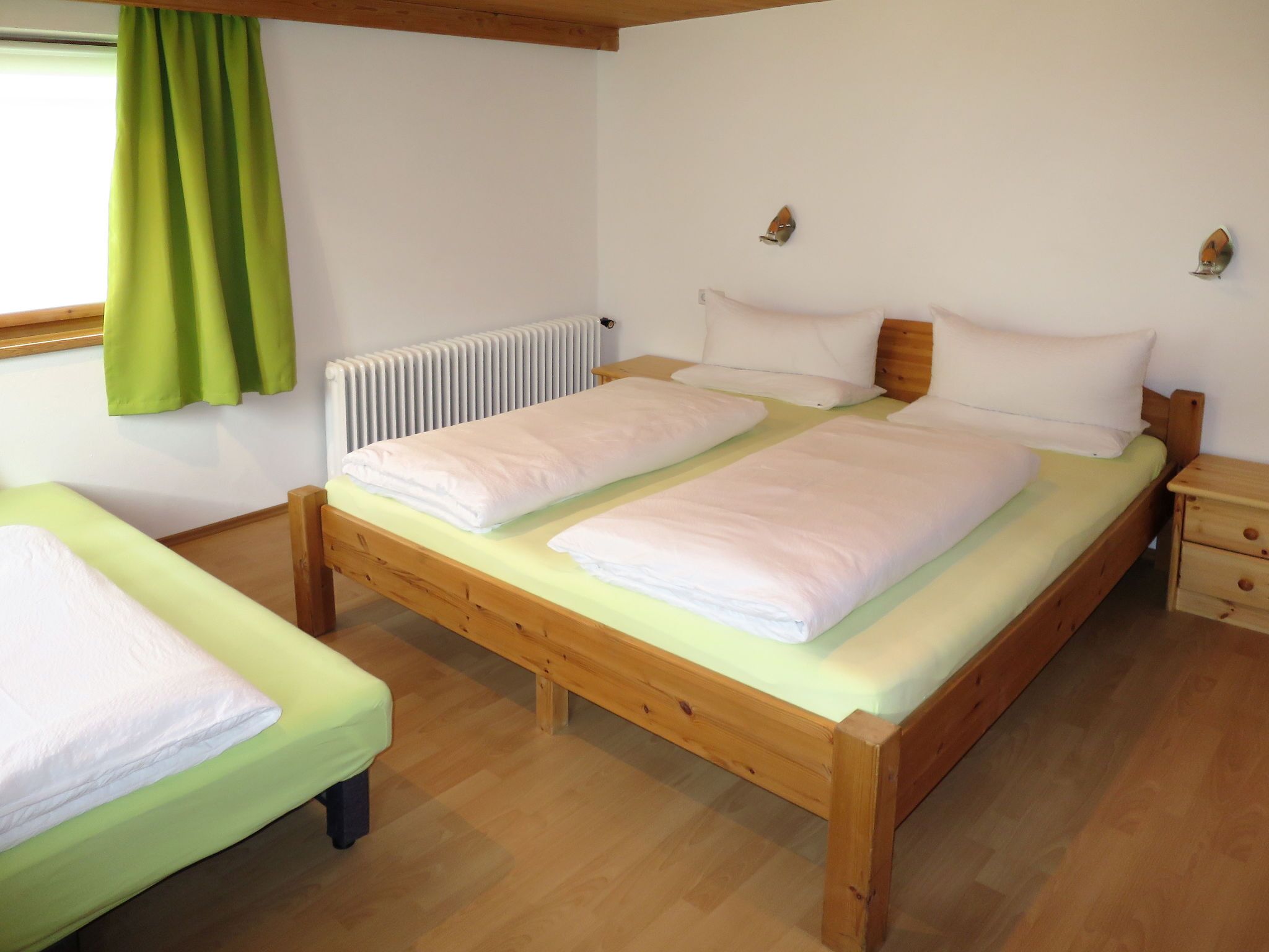 Une chambre avec deux lits en bois, un radiateur et une fenêtre avec des rideaux verts.