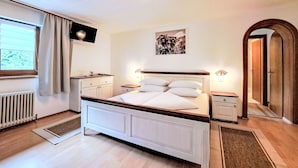 A bedroom with a bed, bedside tables, a radiator, a window with curtains, a wall-mounted TV, and a door. - Gielerhof by Interhome (Zell am Ziller)