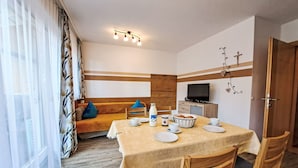 Un comedor acogedor con una mesa lista para dos personas, un sofá con cojines, un televisor y un mueble de madera.