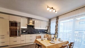 Una cocina moderna con electrodomésticos integrados, un comedor con mesa dispuesta para cuatro personas y ventanas amplias con vistas al exterior.