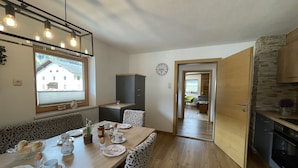 A dining area with a wooden table set for breakfast, a window with blinds, and a view of a building outside.