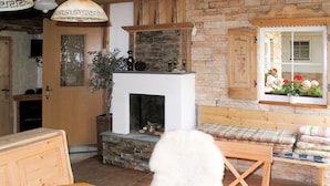 A cozy living room with a fireplace, wooden furniture, and a window with flowers.