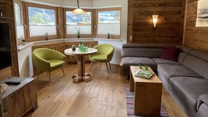 A cozy room with a wooden ceiling, a sofa, two chairs, a small table, and a TV.