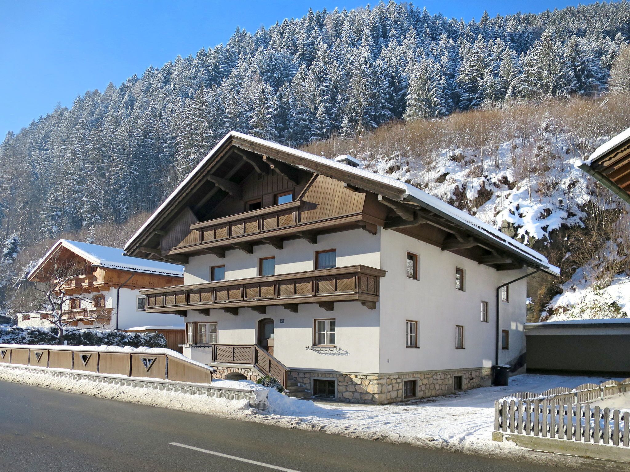Un chalet de dos pisos con base de piedra, balcones de madera y una pista de esquí al fondo.