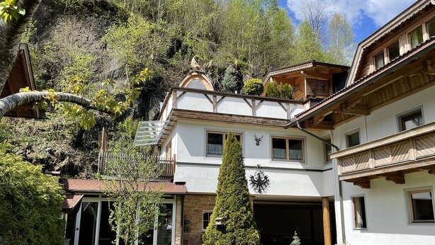 Ein zweigeschossiges Chalet mit geneigtem Dach, einer Garage und einem gepflegten Rasen.