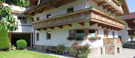 A two-story chalet with wooden balconies, stone foundation, and potted plants.
