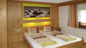 A wooden bedroom with a bed, a nightstand, a wall-mounted picture, and a window with curtains. - Eberharter by Interhome (Zell am Ziller)