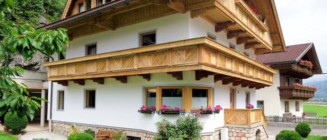 A traditional chalet with a wooden balcony, stone foundation, and a well-maintained garden.