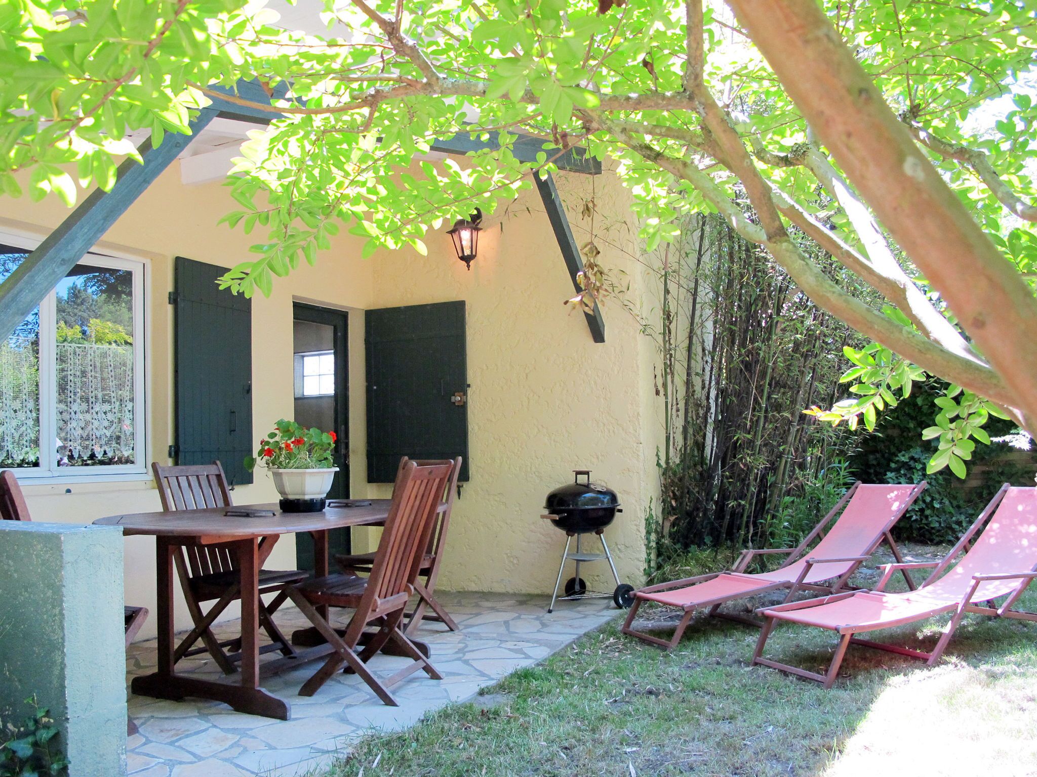 Een terras met een tafel en stoelen, een barbecue en twee loungestoelen onder een boom.