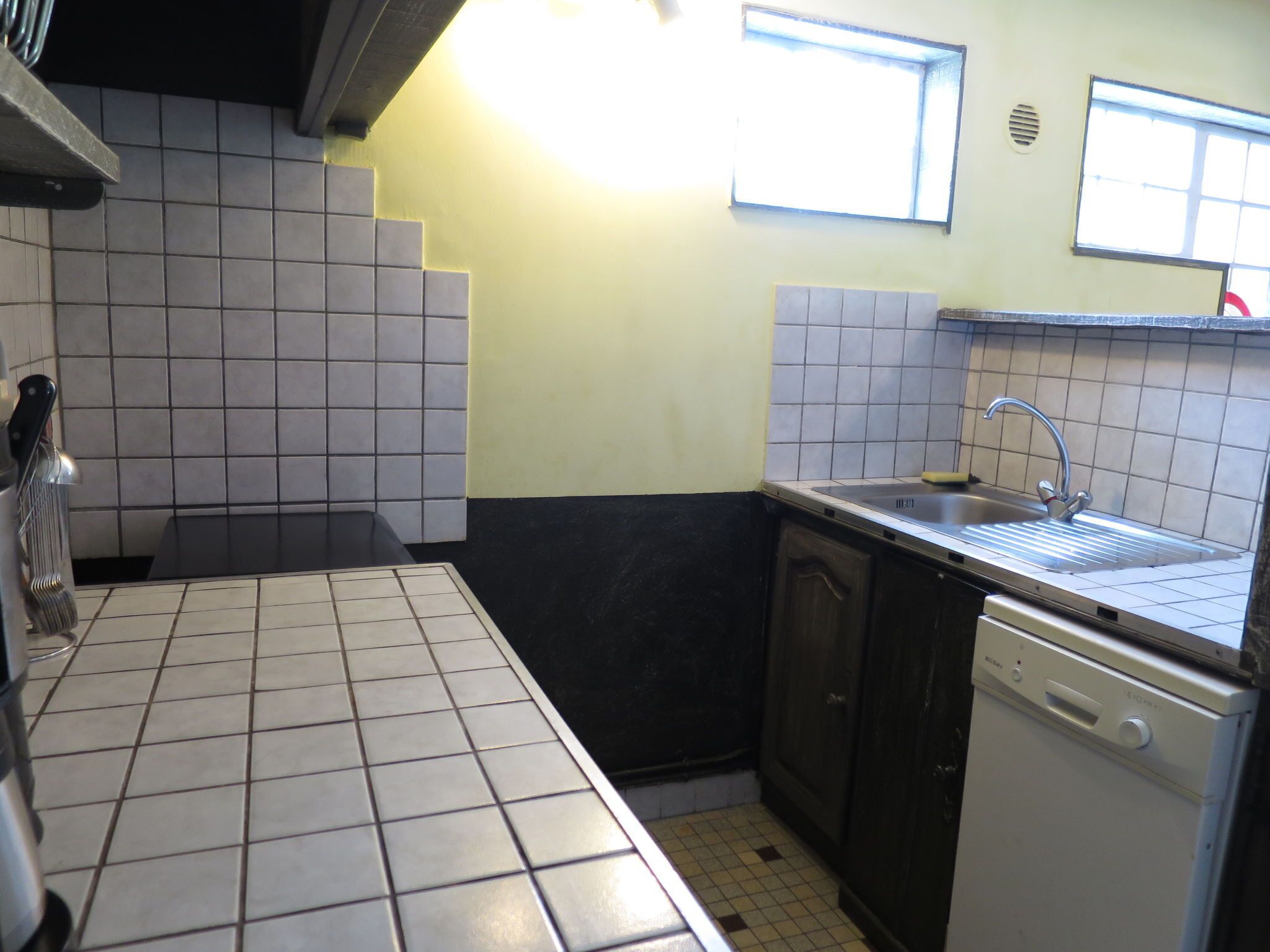 Uma cozinha com azulejos brancos e pretos, uma pia, uma máquina de lavar louça e armários.
