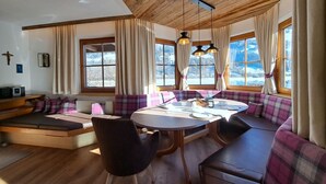 Un coin repas accueillant avec une table ronde, des bancs et une vue sur les montagnes enneigées, visible à travers de grandes fenêtres.