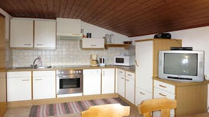 Een functionele keuken met witte kastjes, een magnetron, een fornuis en een televisie op een houten standaard.