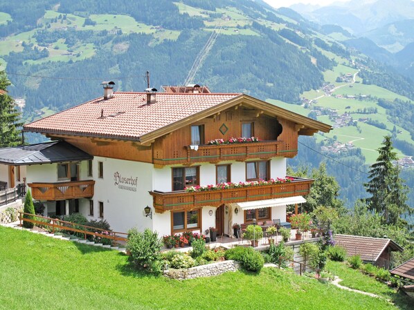 A traditional Alpine-style house with a balcony, a stone staircase, and a garden.