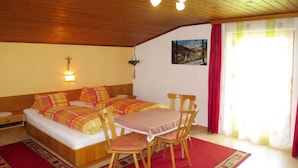 Een knus vertrek met een bed, een tafel met stoelen, een kruis aan de muur en een schilderij.