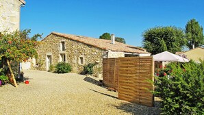 A stone building with a tiled roof, a gravel driveway, and a wooden fence. - Tuilières by Interhome (Pauillac)