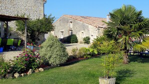 A stone building with a tiled roof, surrounded by a well-maintained garden with various plants and flowers. - Tuilières by Interhome (Pauillac)