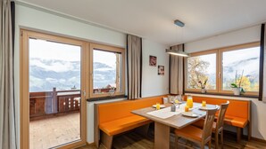 Un comedor con mesa de madera, bancos naranjas y ventanas amplias que ofrecen vistas a la montaña.