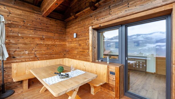 Interior de una cabaña de madera con una mesa, un banco y una ventana con vistas a la montaña.
