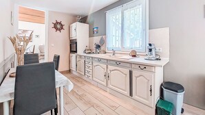 A compact kitchen with a dining area, featuring a built-in oven, a coffee machine, and a large window providing natural light. - L‘Estuaire by Interhome (Begadan)