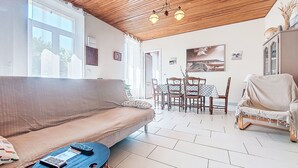 A cozy living room with a wooden ceiling, a sofa, a small round table, and a dining area with chairs and a table. - L‘Estuaire by Interhome (Begadan)