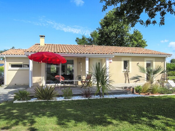 A two-story house with a tiled roof, a patio with outdoor furniture, and a red umbrella.