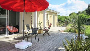 Eine Holzterrasse mit Gartenmöbeln, darunter ein Tisch und Stühle, sowie ein roter Sonnenschirm.