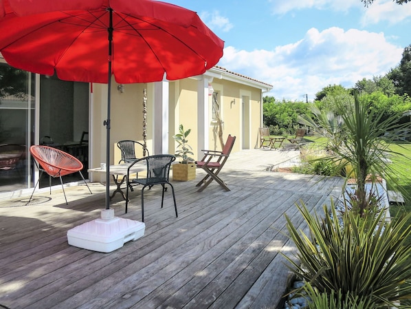 A wooden deck with outdoor furniture, including a table and chairs, and a red umbrella.