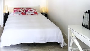 Ein ordentlich bezogenes Bett mit weißer Bettwäsche und dekorativen Kissen, zwei Nachttischlampen und ein weißer Nachttisch mit einem schwarzen Gegenstand darauf.