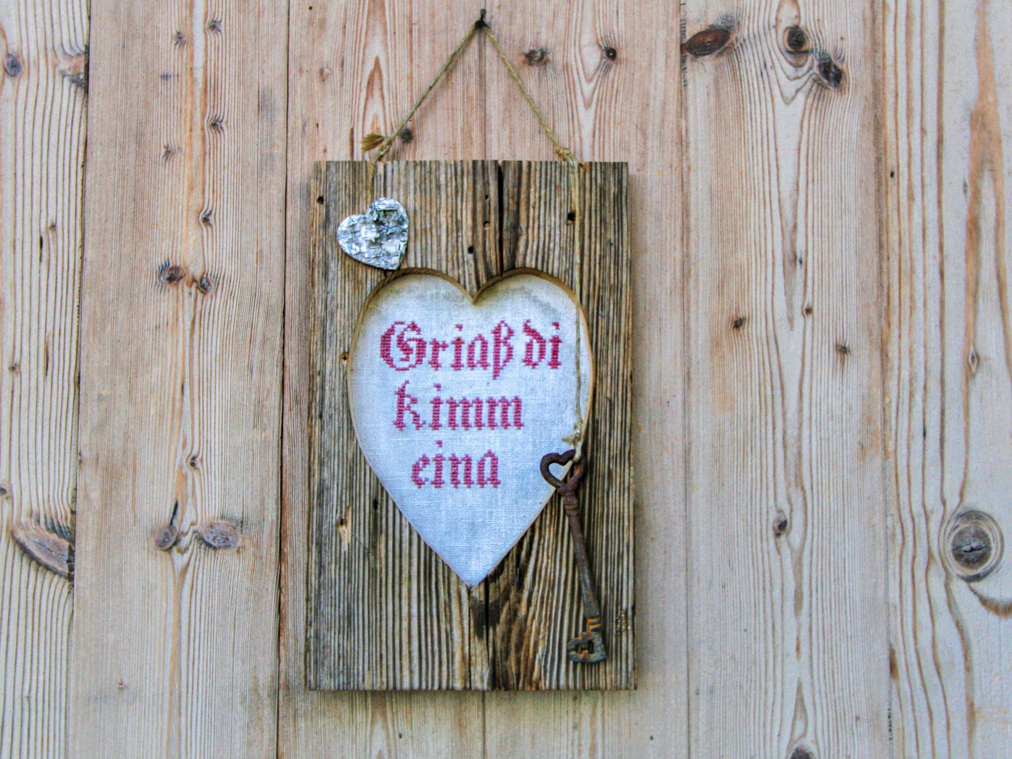 A wooden heart-shaped sign with a heart-shaped cutout and a keyhole, hanging on a wooden wall.
