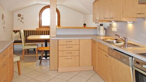 A kitchen with wooden cabinets, a built-in oven, a coffee maker, and a dining area with a bench and table. - Unterkreuter by Interhome (Kaltenbach)