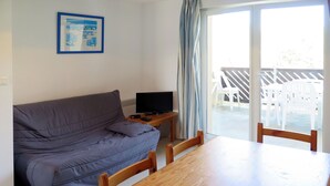 Een kamer met een bank, een televisie, een houten tafel en uitzicht op terrasstoelen.