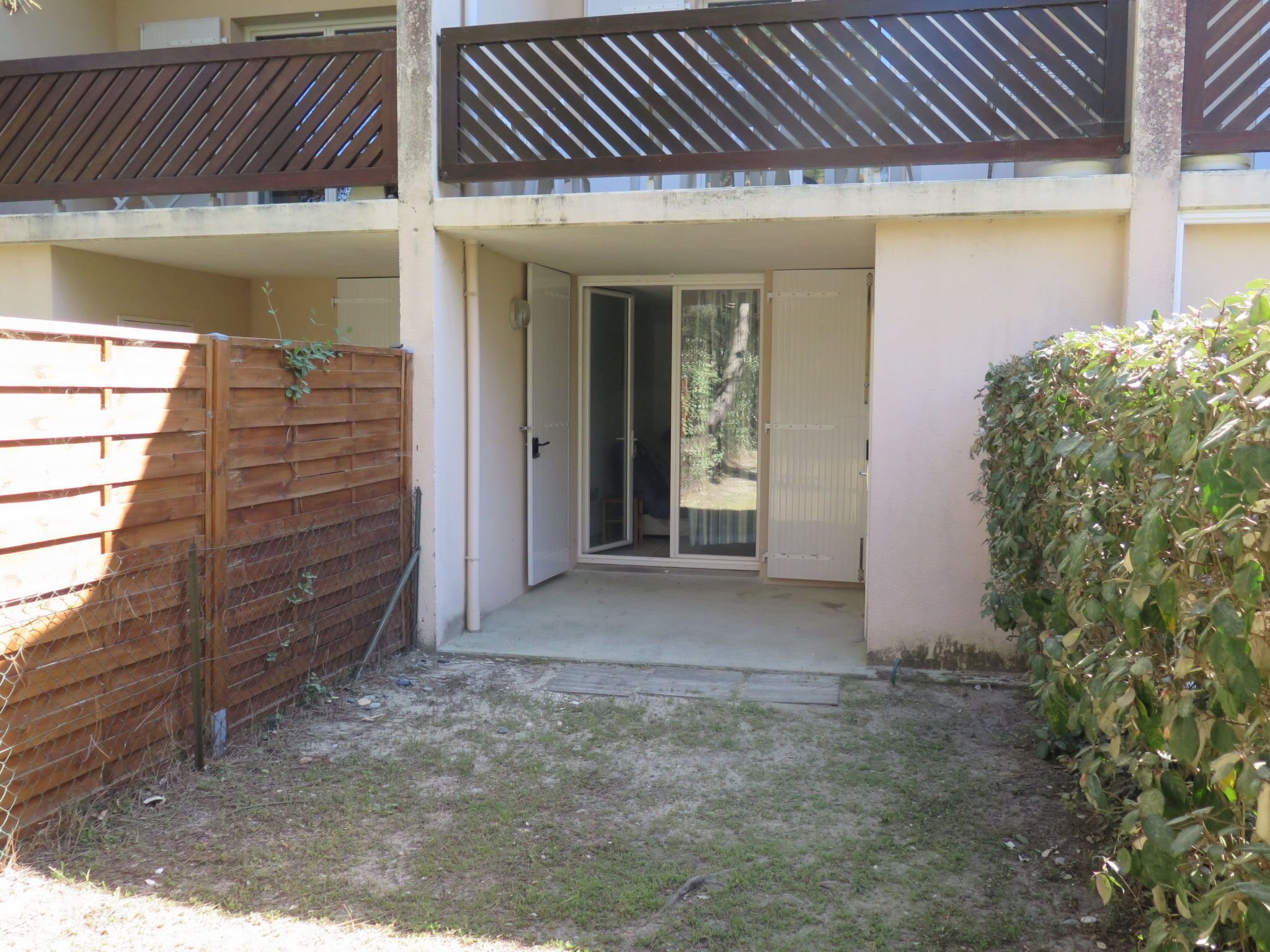 A residential building with a small front yard, a wooden fence, and a sliding glass door leading to a balcony.
