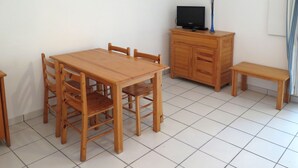 A room with a wooden dining table, four chairs, a small wooden cabinet with a television, and a bench. - Les Hameaux de l'Océan 22 by Interhome (Carcans Plage)