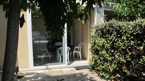 A patio area with a glass door leading to a room, a white chair, and a hedge. - Les Hameaux de l'Océan 22 by Interhome (Carcans Plage)
