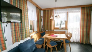 Ein gemütlicher Essbereich mit einem Holztisch und Bänken, umgeben von karierten Vorhängen und einem an der Wand befestigten Fernseher.