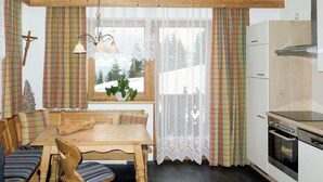 Eine gemütliche Küche mit Holztisch, Bank und Blick auf verschneite Berge durch das Fenster.